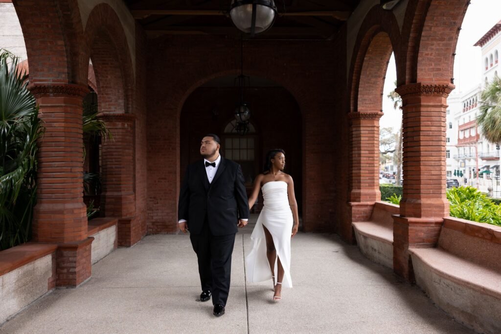 A couple in formal attire walking under beautiful red brick arches