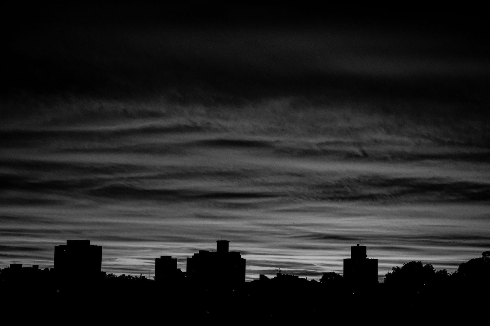A dramatic black and white city skyline silhouette with a moody twilight sky