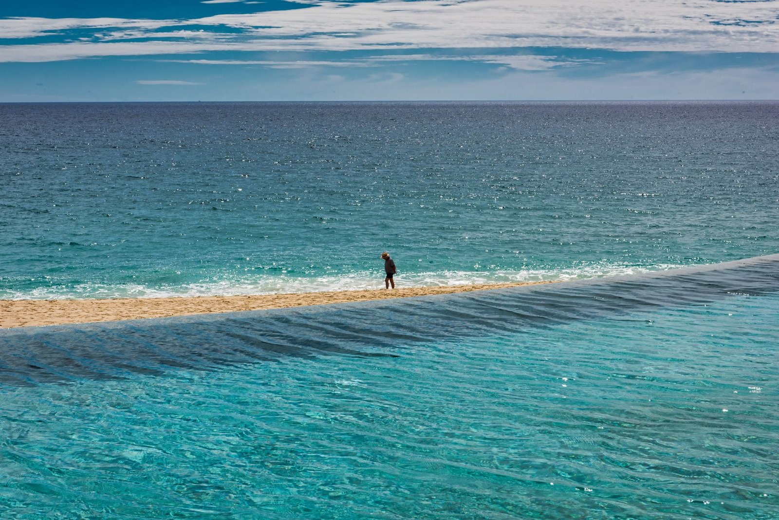 A lone person strolls along the serene beach in San José del Cabo, Mexico under a bright blue sky