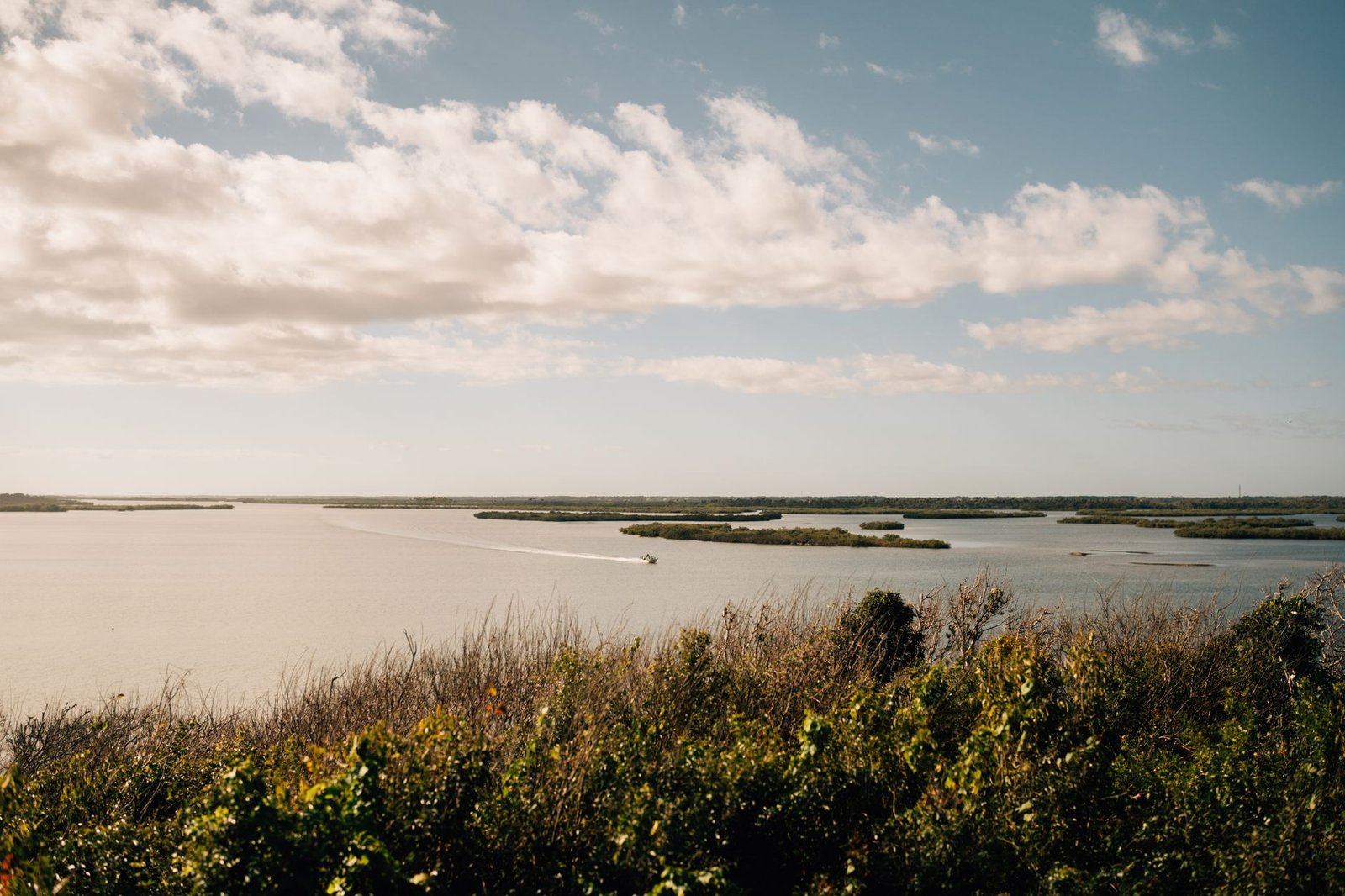 A peaceful rural landscape with a motorboat cruising on a calm lake under a cloudy sky