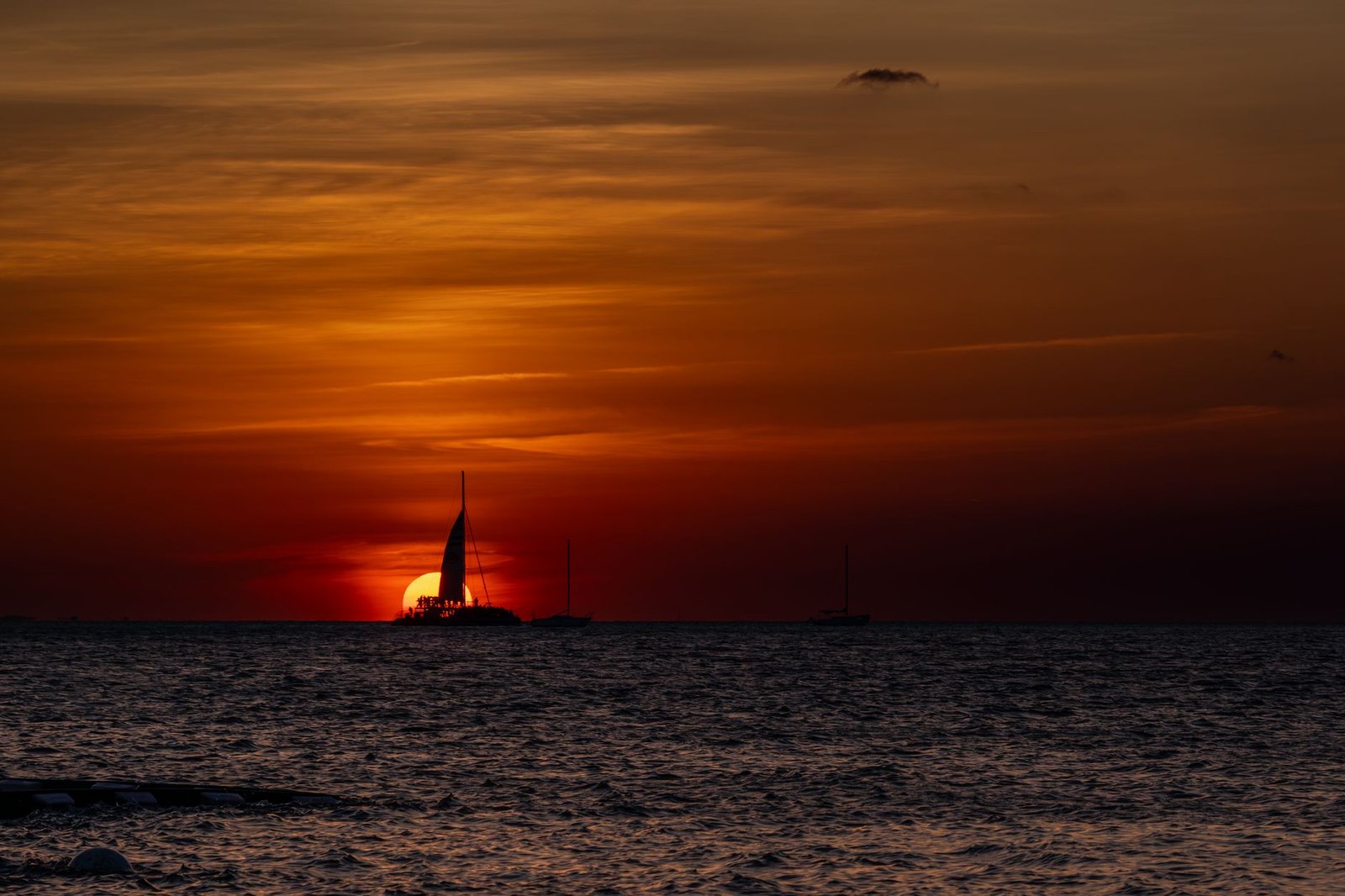 A sailboat silhouetted against a vibrant sunset over the ocean in Cayo Hueso, Florida