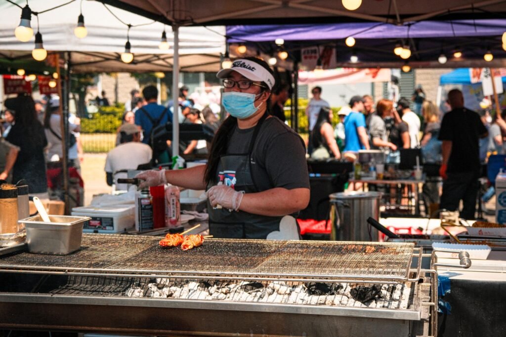 A street food vendor grilling skewers at an outdoor market in Toronto during a sunny summer day