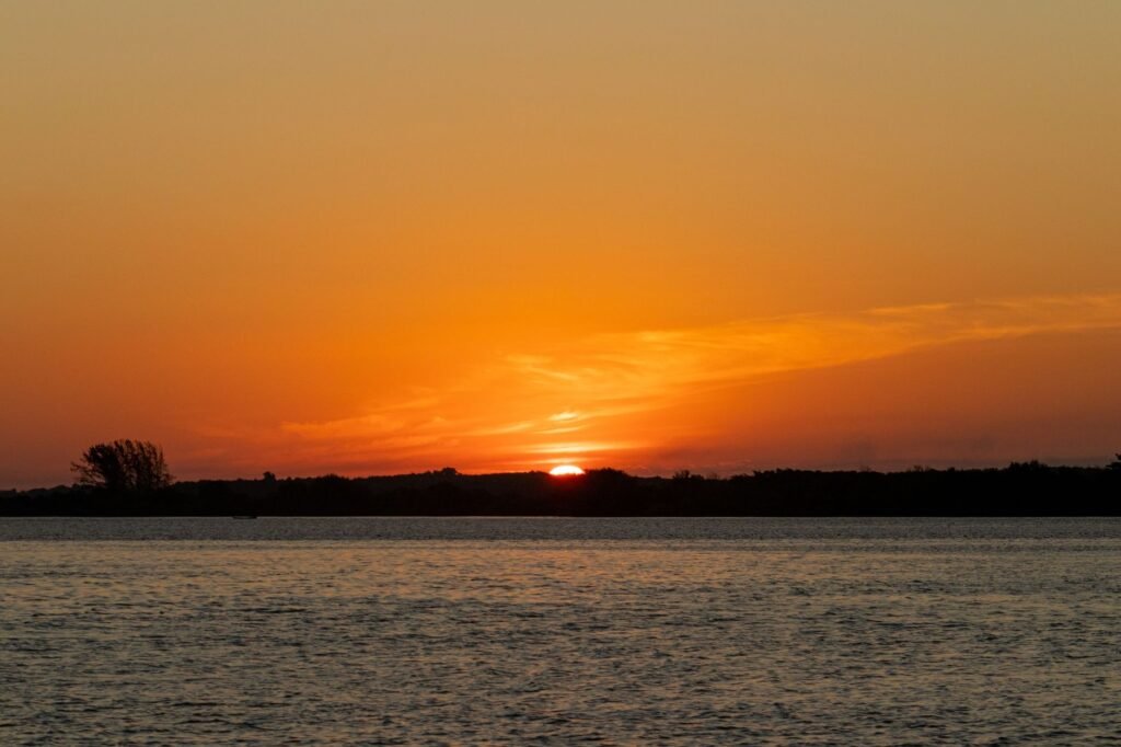 Beautiful sunset over a tranquil lake in Brazil, casting silhouettes of distant trees