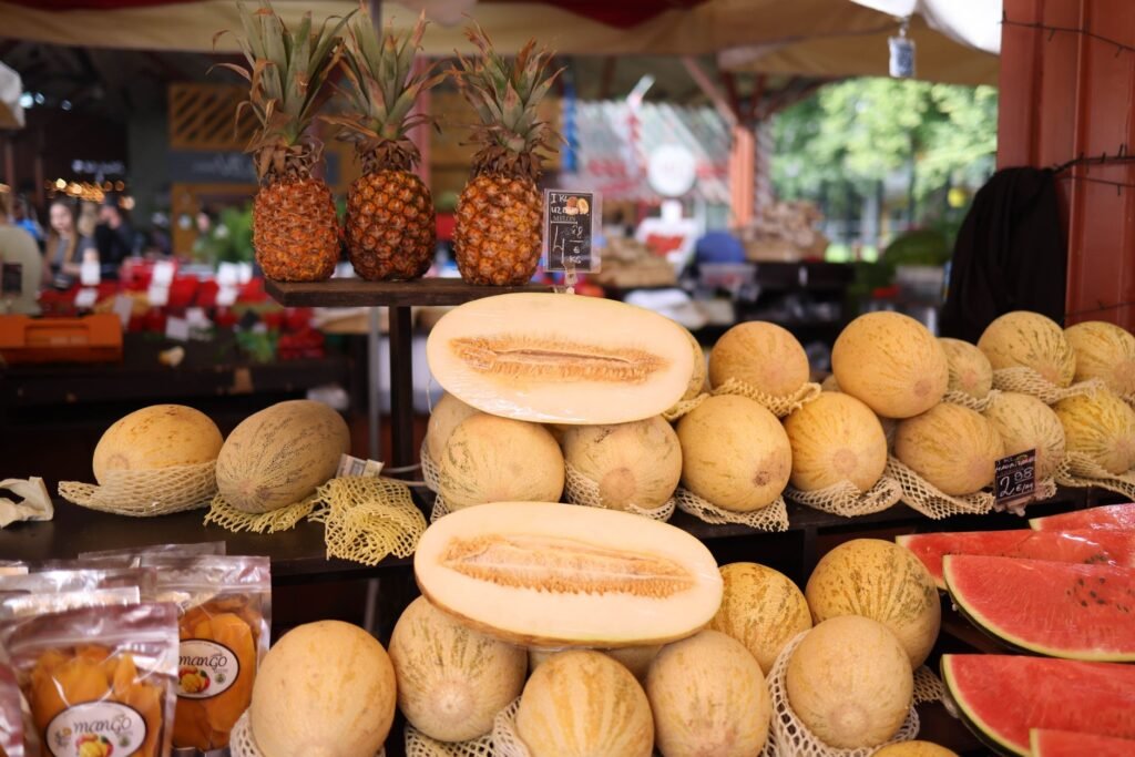 Colorful display of fresh melons, pineapples, and watermelons at an outdoor market stall
