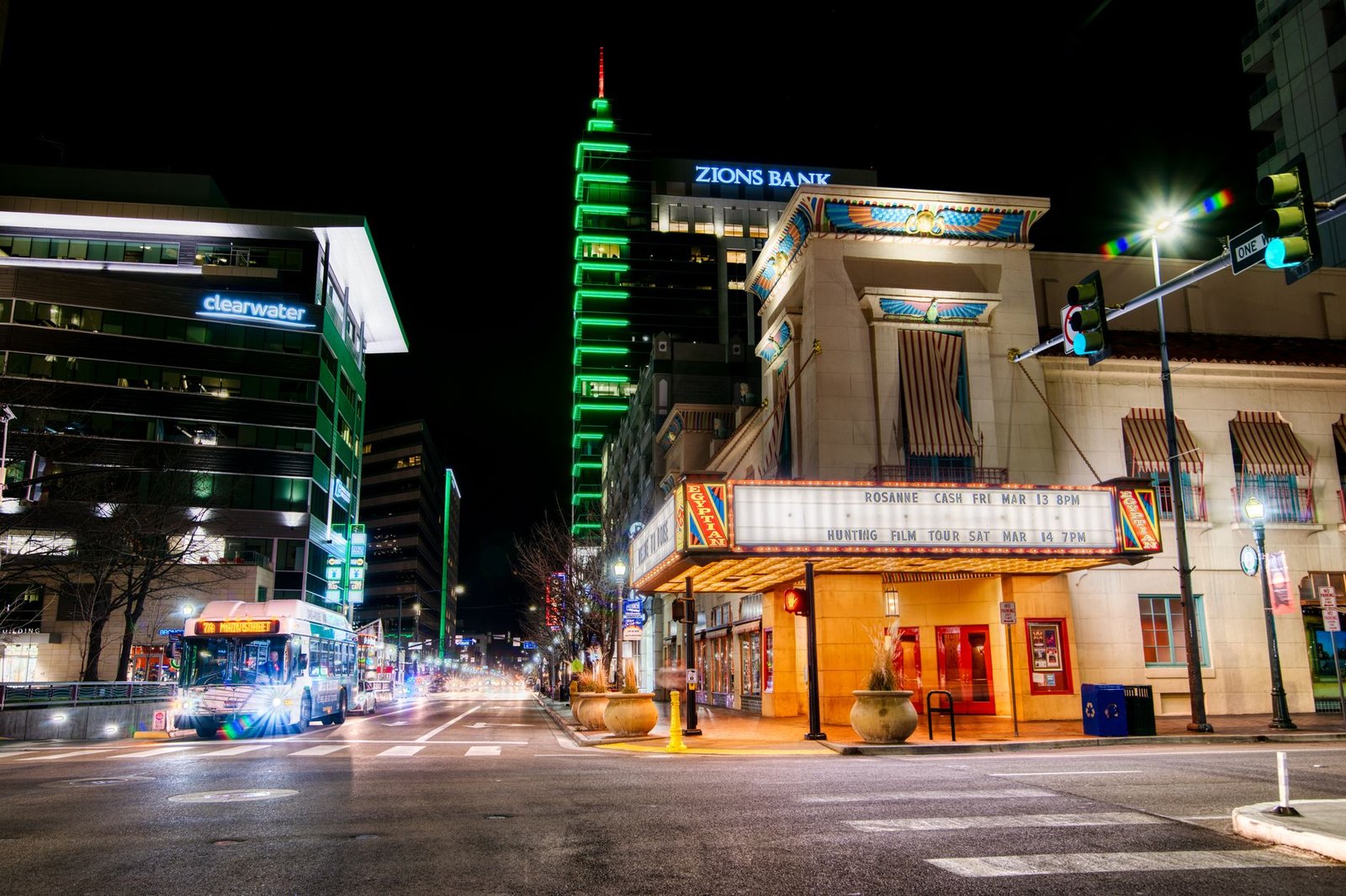 Contemporary city district street with moving vehicles on road near modern buildings illuminated by bright lights in late evening
