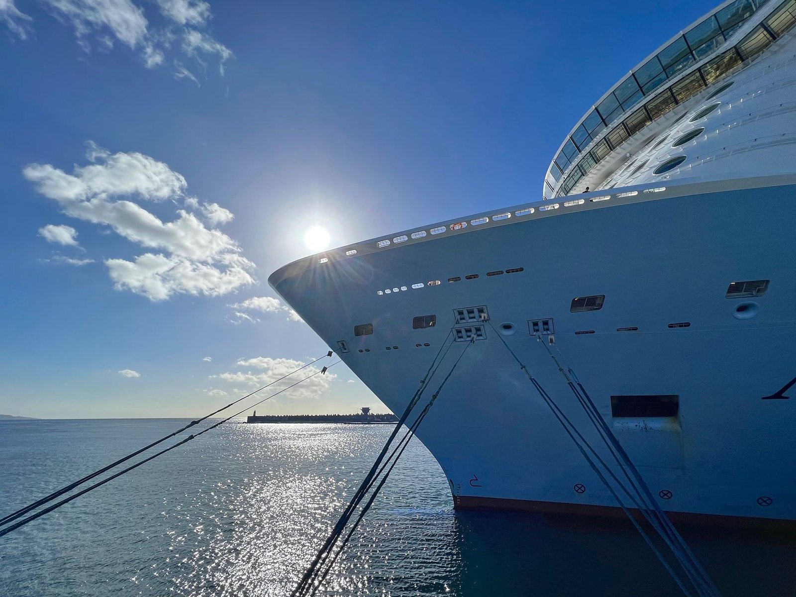 Cruise ship docked at Ponta Delgada terminal under a bright sky with sun glistening on the ocean