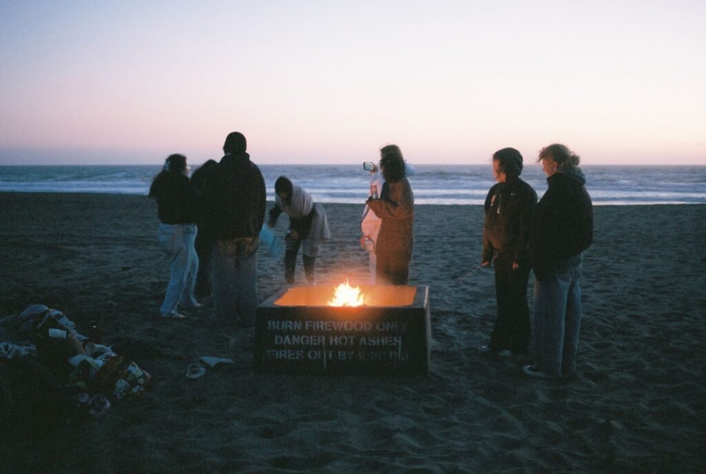 Group of people enjoying a cozy bonfire by the beach at dusk