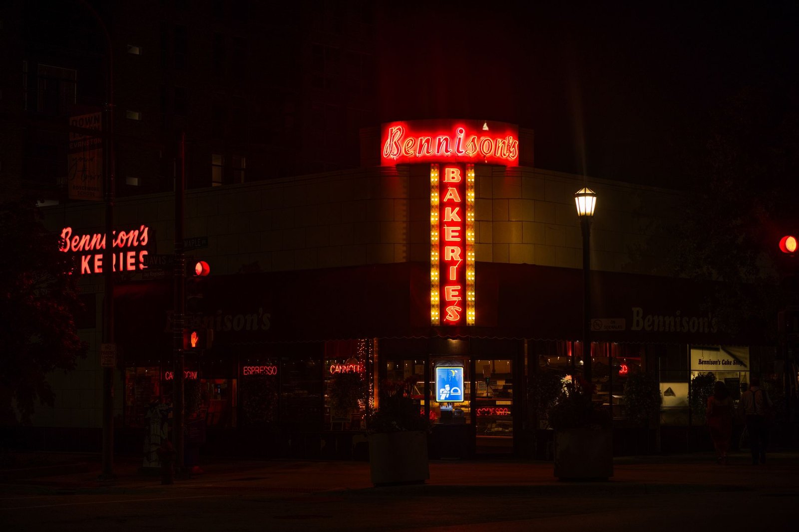 Illuminated neon sign of Bennison's Bakery at night on a dark urban street