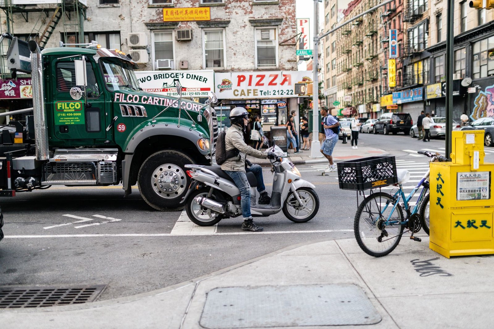 Motorcycle rider waits at a crossroad in a busy urban street with a large truck and city buildings in the background