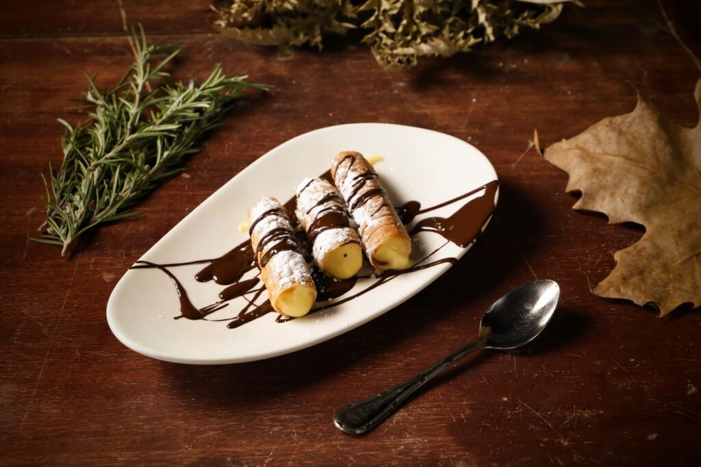 Plate of cannoli filled with cream and drizzled with chocolate, served with herbs