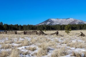 Tranquil view of snow-dusted Kendrick Peak with a rustic wooden fence in Arizona's serene landscape